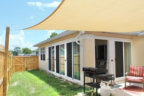 Ein Haus mit Terrasse, Grill und überdachter Sitzgelegenheit.