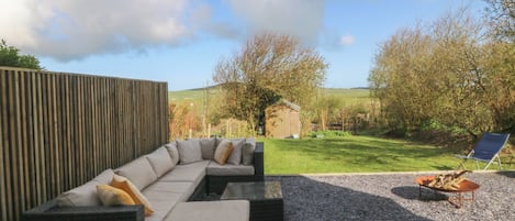 A curved outdoor seating area with cushions, a small fire pit, and a wooden fence.