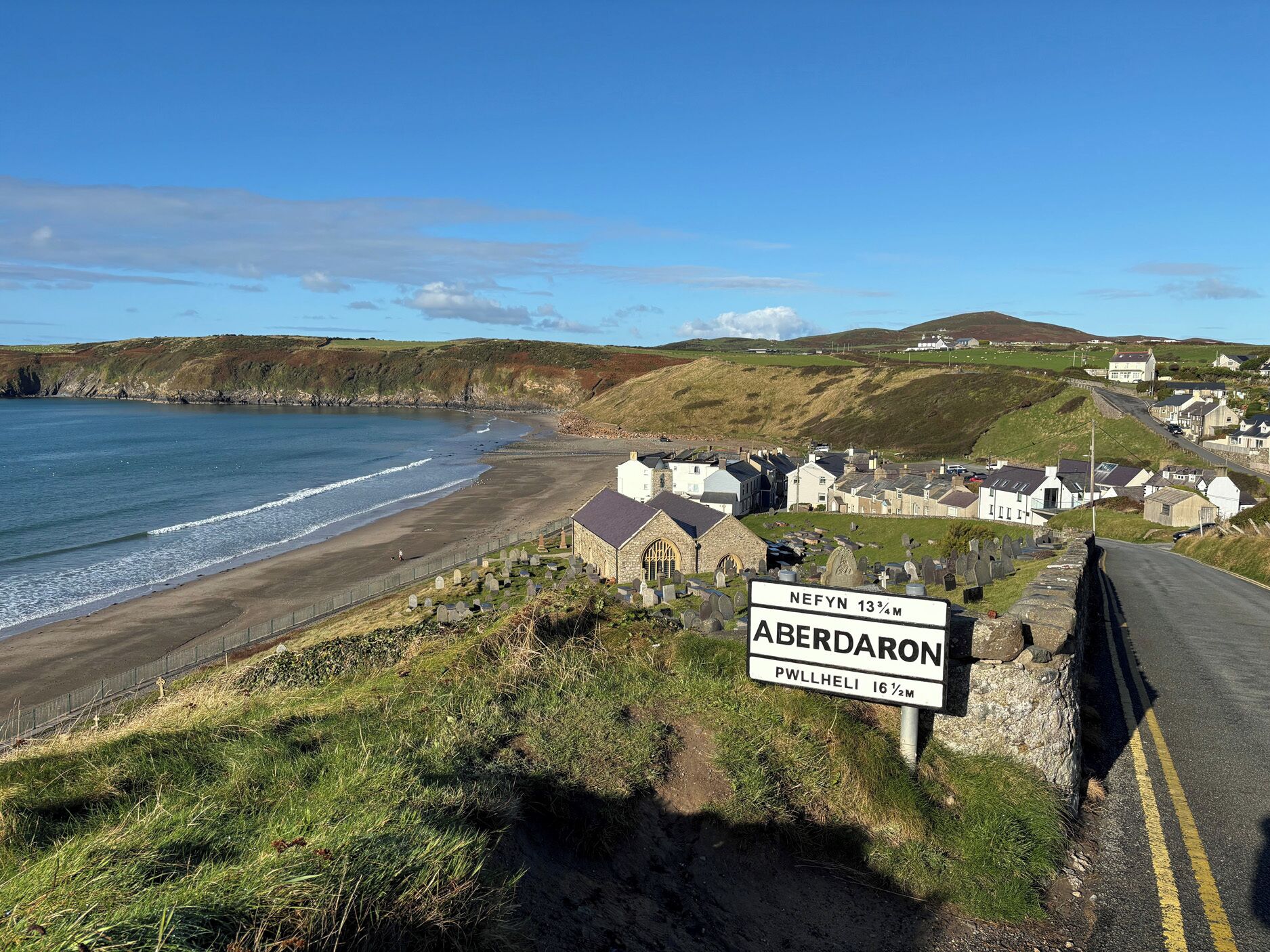 A coastal road with a sign indicating the distance to Aberdaron and Pwllheli.