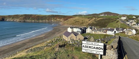 A coastal road with a sign indicating the distance to Aberdaron and Pwllheli.