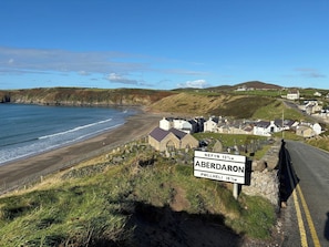 Eine Küstenstraße mit einem Schild, das die Entfernung nach Aberdaron und Pwllheli angibt.