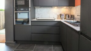 Una cocina moderna con armarios oscuros, horno empotrado y hervidor de acero inoxidable.