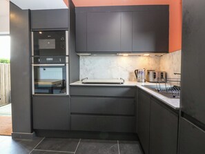 Eine moderne Küche mit dunklen Schränken, einem eingebauten Backofen und einem Edelstahl-Wasserkocher.