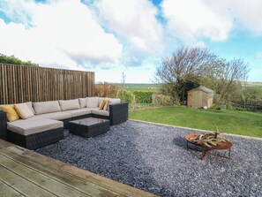 Eine Terrasse mit einer Eckcouch, einem kleinen Tisch und einer Schubkarre mit Pflanzen.