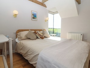 Ein Schlafzimmer mit Bett, Kissen, Nachttisch, Fenster mit Blick und Heizkörper.