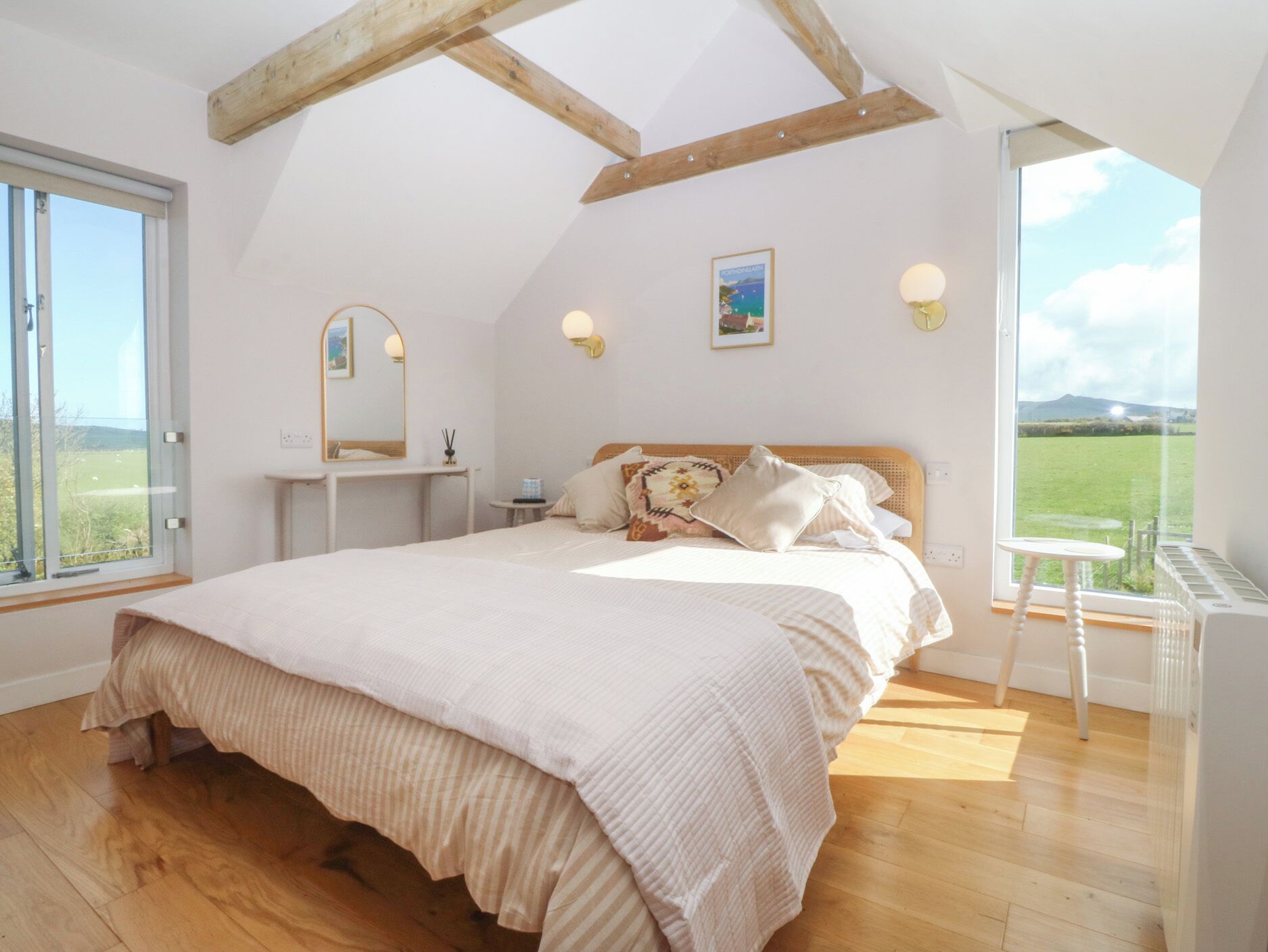 A bedroom with a large bed, a bedside table, a mirror, and a view of a green landscape.