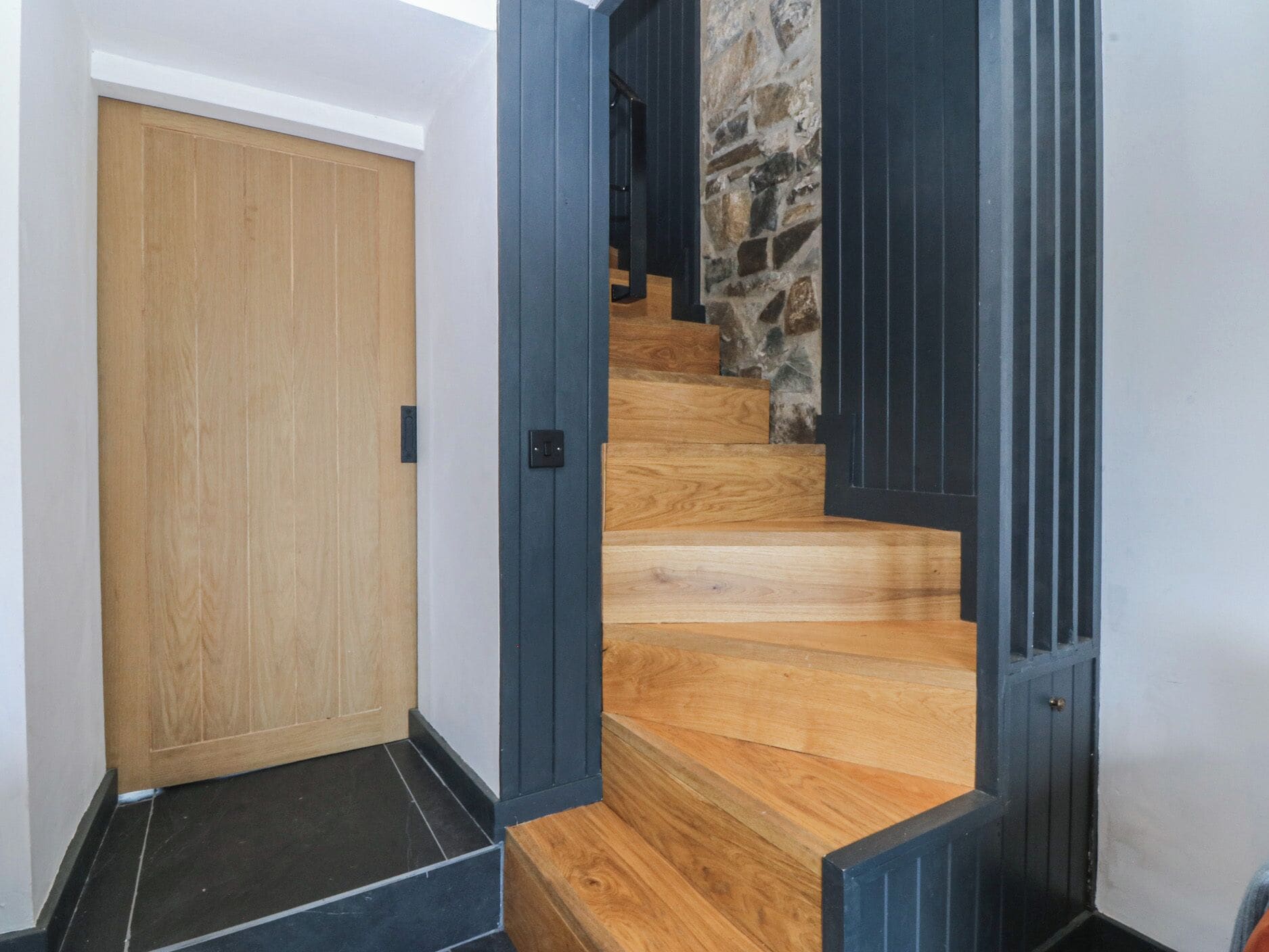 A wooden staircase with a stone wall, a wooden door, and a black floor.