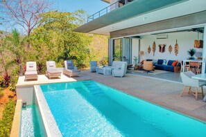 Ein moderner Poolbereich mit Liegestühlen, einer Sitzecke und einem Esstisch.