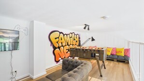 Una sala de estar con una mesa de fútbol de mesa, un sofá y una pared con grafitis.