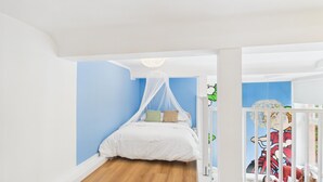 Un dormitorio con cama, dosel blanco, paredes azules, suelo de madera y baranda blanca.