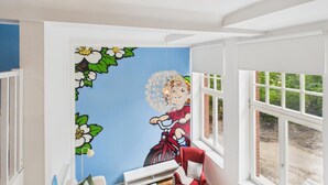Una habitación con un mural de un personaje de caricatura, una ventana que da a zonas verdes y una silla roja.