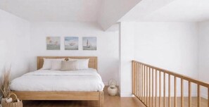 Ein Schlafzimmer mit einem hölzernen Bett, weißer Bettwäsche, einem kleinen Nachttisch und einem Beistelltisch. An der Wand hängen drei Bilder von Segelbooten.