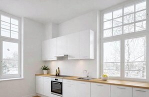Eine moderne Küche mit weißen Schränken, einer Holz Arbeitsplatte, einem eingebauten Backofen und großen Fenstern.