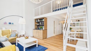 Een modern appartement met een slaapkamer op een entresol, een keuken met houten kasten, een eethoek en een trap.