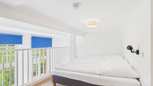 Un dormitorio con cama, ventana con persianas, balcón y lámpara en el techo.
