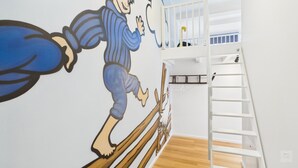 Una habitación con techo alto, piso de madera, barandal blanco y un mural en la pared.