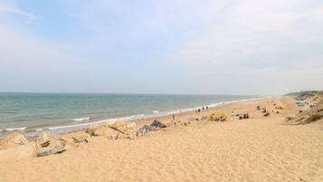 A sandy beach with a clear sky, rocky outcrops, and people enjoying the area.