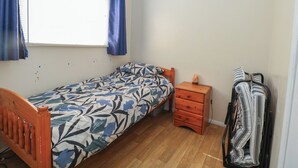 A small bedroom with a single bed, a nightstand, a heater, and a coat rack. - Mon Chalet (Great Yarmouth)