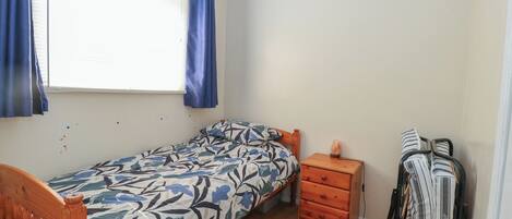 Un dormitorio pequeño con una cama individual, una mesita de noche, un calentador y un perchero.