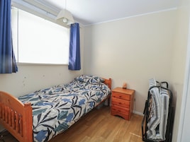 Un dormitorio pequeño con una cama individual, una mesita de noche, un calentador y un perchero.