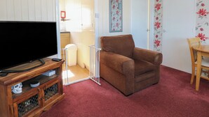 A living room with a television, a brown chair, a wooden table, and a red carpet. - Mon Chalet (Great Yarmouth)