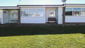 A single-story mobile home with a front porch, a satellite dish, and a small bench. - Mon Chalet (Great Yarmouth)