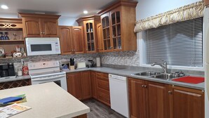 Una cocina con armarios de madera, microondas, estufa, lavavajillas y una ventana con persianas.