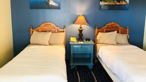 Ein Hotelzimmer mit zwei Betten, einem Nachttisch mit Lampe sowie zwei gerahmten Bildern an der Wand.