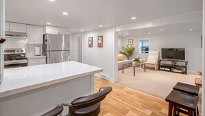 Una cocina moderna con armarios blancos, una isla grande y una zona de comedor con televisión y asientos.