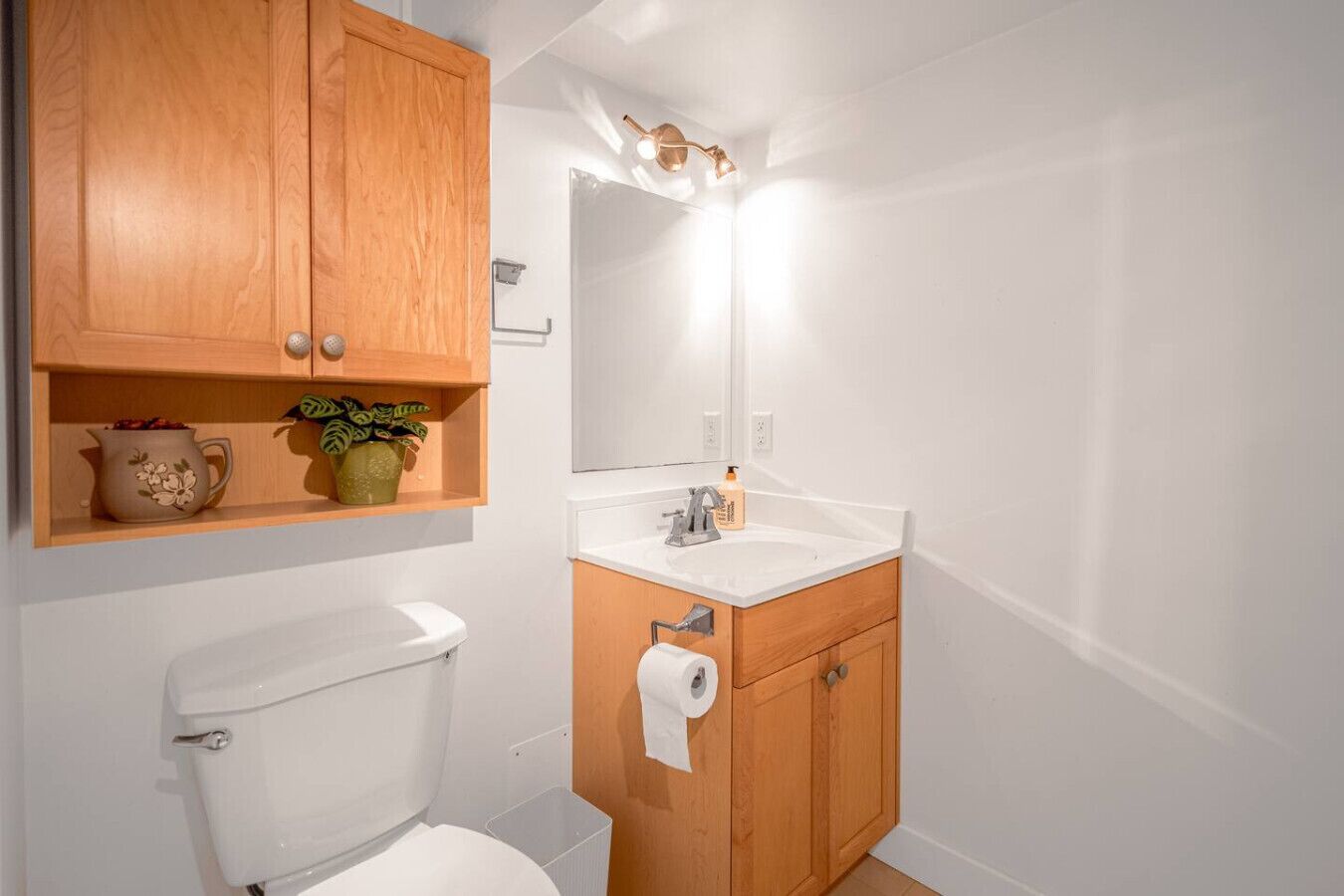 A bathroom with a toilet, wooden cabinets, a sink, and a mirror.