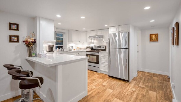 Una cocina moderna con armarios blancos, electrodomésticos de acero inoxidable y una isla central con taburetes de bar.
