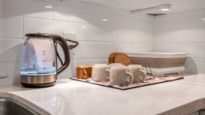 Una cocina con una tetera, tazas y un colador sobre la encimera.