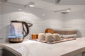 Une cuisine équipée d’une bouilloire, de tasses et d’une passoire sur le plan de travail.
