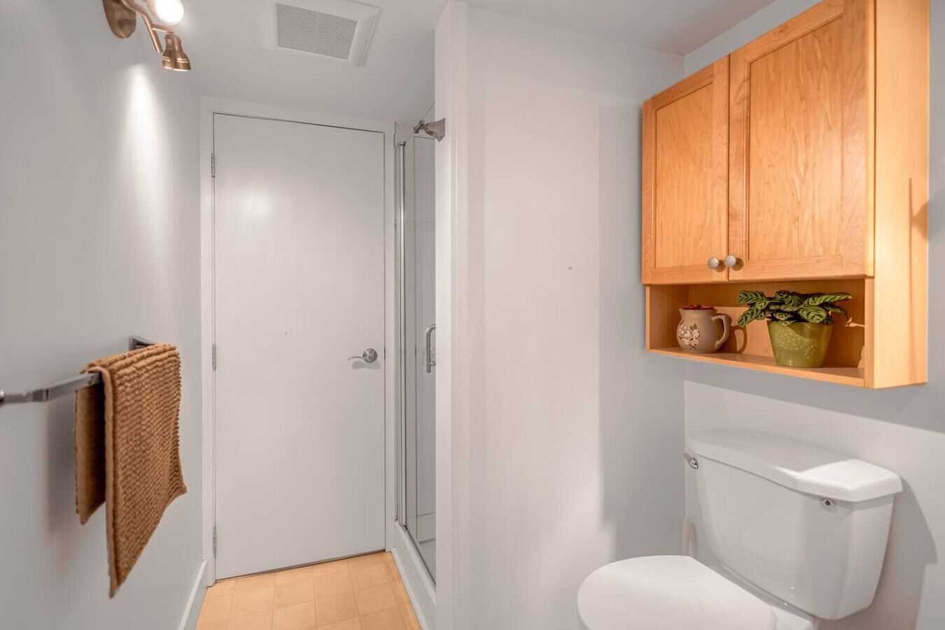 Un baño con inodoro, cabina de ducha y un mueble de madera sobre el inodoro.