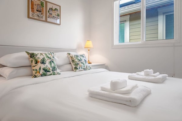 Ein Hotelzimmer mit Bett, Kissen, einem Nachttisch mit Lampe und einem Fenster mit Jalousien.