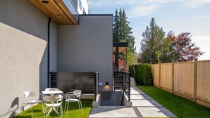 Un patio moderno al aire libre con un camino de concreto, una cerca de madera y un pequeño espacio de estar con sillas.