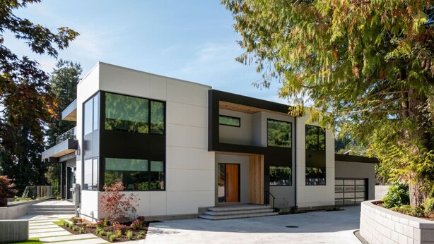 Una casa moderna de dos pisos con amplios ventanales, una puerta principal y un camino de acceso.