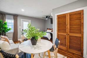 Ein Zimmer mit rundem Tisch, einem Blumentopf, einem Bett mit gemustertem Kopfteil und einem hölzernen Kleiderschrank.