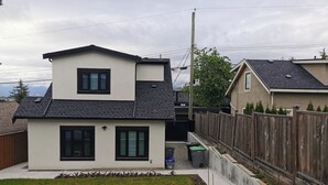 Een tweelaags huis met een schuin dak, een omheinde achtertuin en een zichtbare afvalcontainer.