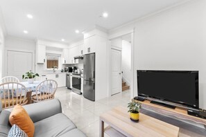 A modern kitchen with white cabinets, a stainless steel refrigerator, and a dining area with a table and chairs. - Modern Private 3BR House Vancouver (Vancouver)
