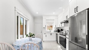 Een moderne keuken met witte kasten, roestvrijstalen apparatuur en een eethoek met een tafel en stoelen.