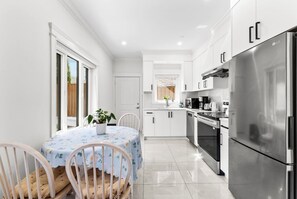 A modern kitchen with white cabinetry, stainless steel appliances, and a dining area with a table and chairs. - Modern Private 3BR House Vancouver (Vancouver)
