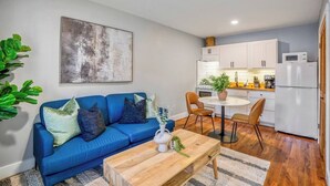A living room with a blue sofa, a wooden coffee table, and a kitchen area with white cabinets and a microwave. - Urban Retreat Near Downtown Houston with Gated Access (Houston)