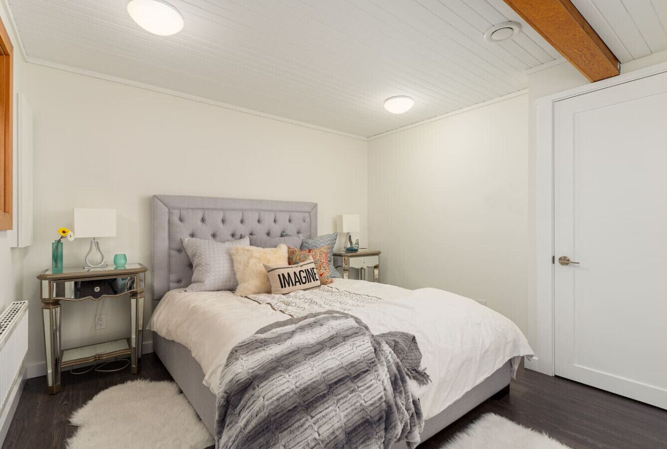 A bedroom with a bed, nightstands, a white door, and a ceiling with recessed lighting.
