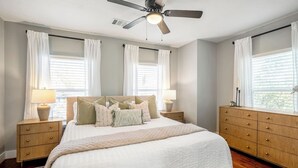 A bedroom with a bed, two nightstands, a dresser, a ceiling fan, and a window with blinds. - Spacious 2BR Home with King Beds Near Downtown, WiFi, Parking & Easy Self Check-In (Houston)