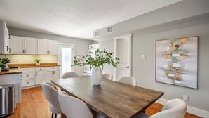 A modern kitchen with white cabinets, a wooden countertop, and a dining area with a wooden table and chairs. - Spacious 2BR Home with King Beds Near Downtown, WiFi, Parking & Easy Self Check-In (Houston)