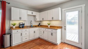 A kitchen with white cabinets, a wooden countertop, a sink, and a window with blinds. - Spacious 2BR Home with King Beds Near Downtown, WiFi, Parking & Easy Self Check-In (Houston)
