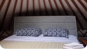 Una struttura circolare in legno con un letto e cuscini, un lucernario e vista sugli alberi.