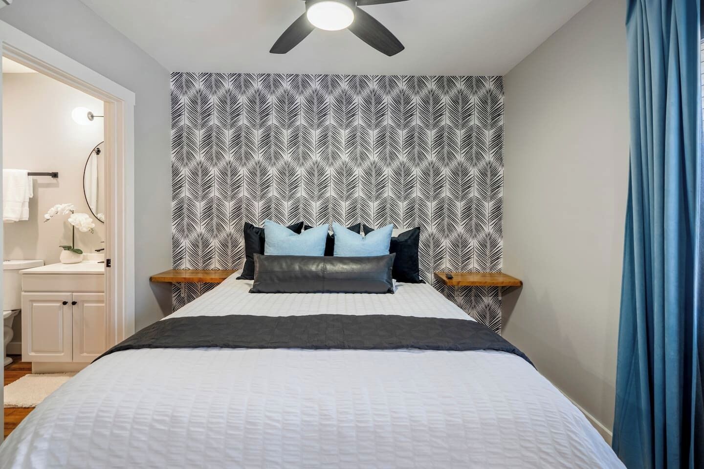 Une chambre à coucher avec un papier peint à motifs, un lit avec des oreillers, un ventilateur de plafond et une table de chevet.
