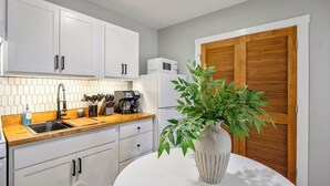 Une cuisine avec des meubles blancs, un plan de travail en bois, une machine à café et une plante en pot.